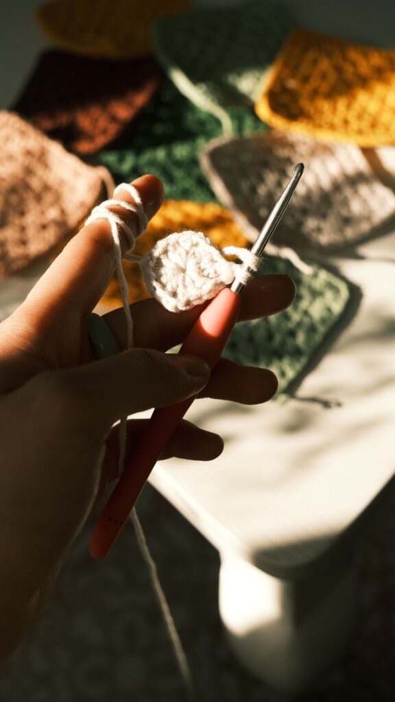 Imagem atual: Hand holding crochet hook creating vibrant squares in sunlight.